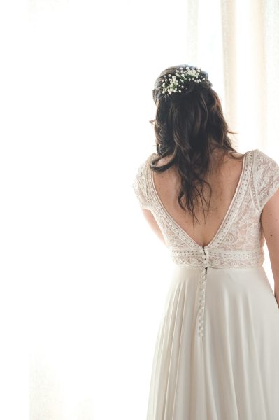 Une mariée habillée en robe blanche regarde par la fenêtre juste avant son mariage